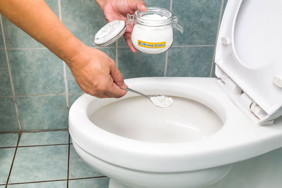 Pouring baking soda and vinegar into a toilet bowl to unclog it