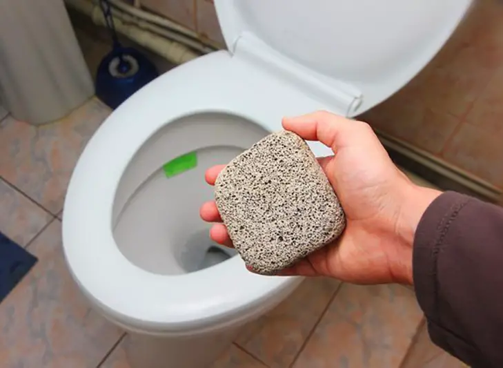 Cleaning a toilet bowl with a pumice stone